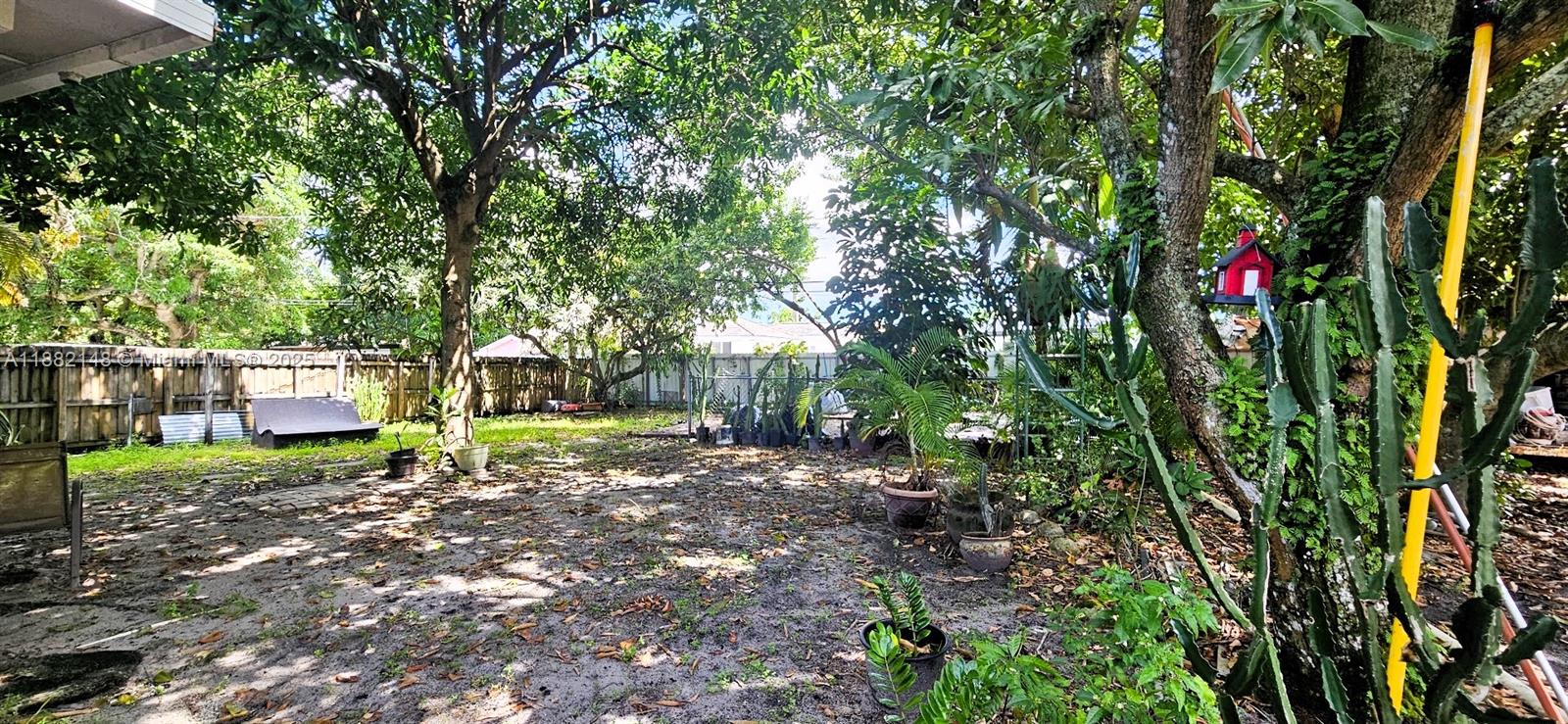 A backyard features a dirt ground, mature trees, potted plants, and a wooden fence — 243 NW 62nd Ct, Miami FL 33126, MIAMI, FL
