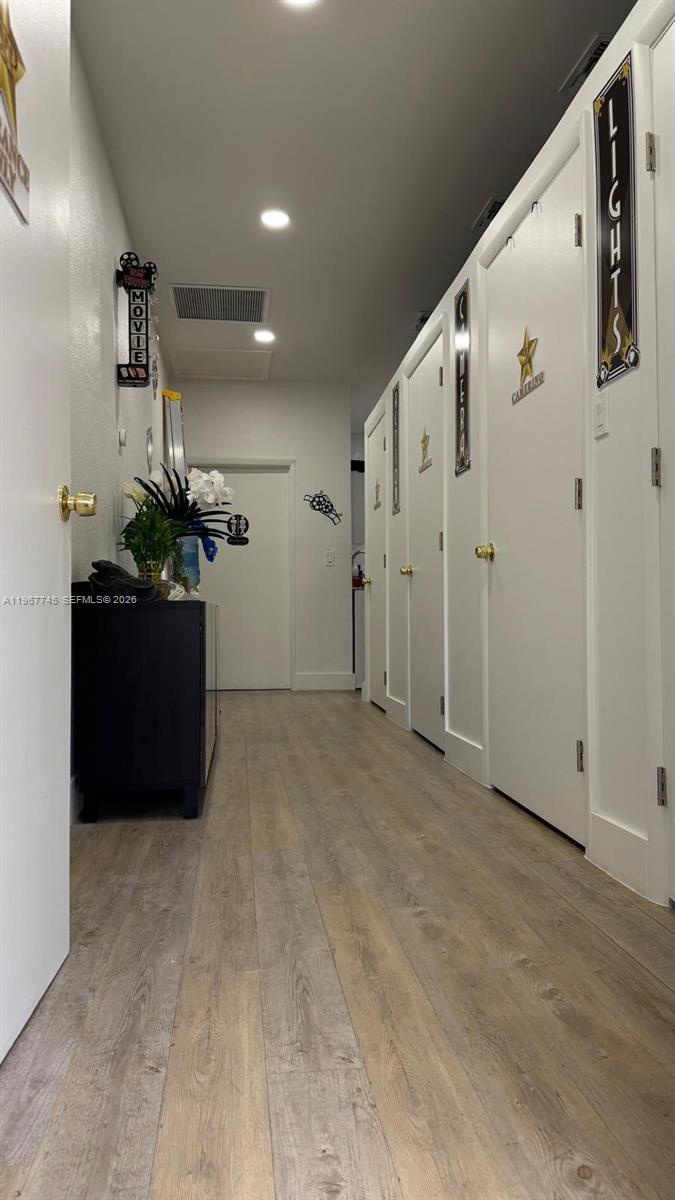 A hallway features light wood-look flooring, white doors with decorative signs, and a black cabinet — 213 Park Blvd, Miami FL 33126, MIAMI, FL