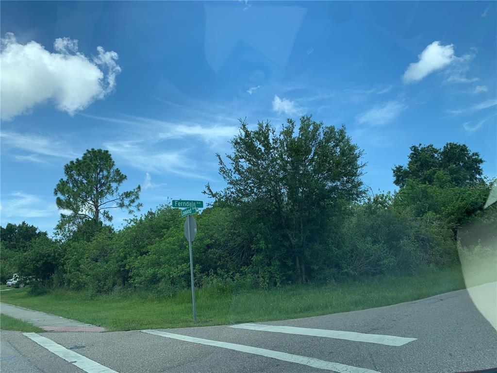 A street sign for Ferndale Avenue stands at a corner lot with trees and grass — 2035 LOVELAND BOULEVARD, PORT CHARLOTTE, FL