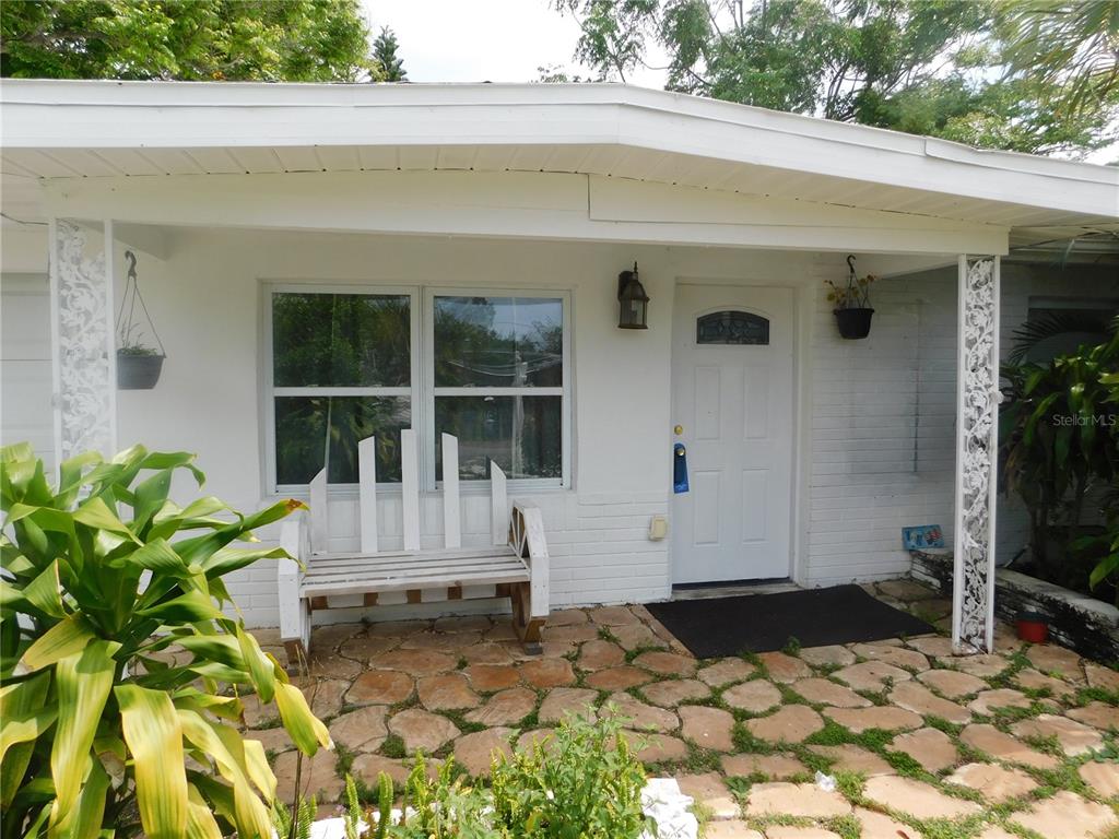 A white house exterior features a stone patio, a wooden bench, and decorative metal columns — 4542 BELFAST DRIVE, NEW PORT RICHEY, FL