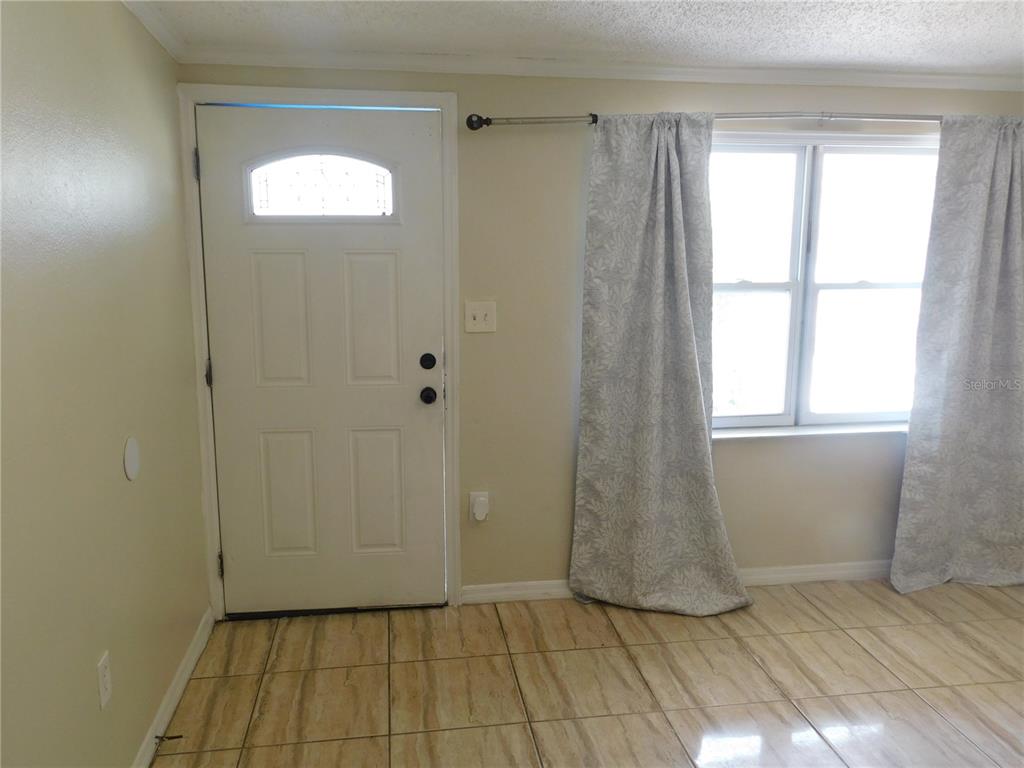 A room with a white front door, a window with patterned curtains, and tiled flooring — 4542 BELFAST DRIVE, NEW PORT RICHEY, FL