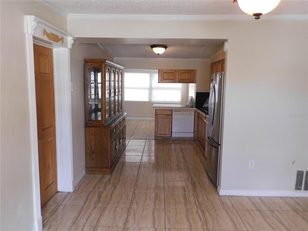 A kitchen with wood cabinets, stainless steel appliances, and tiled floors leads to a dining area — 4542 BELFAST DRIVE, NEW PORT RICHEY, FL