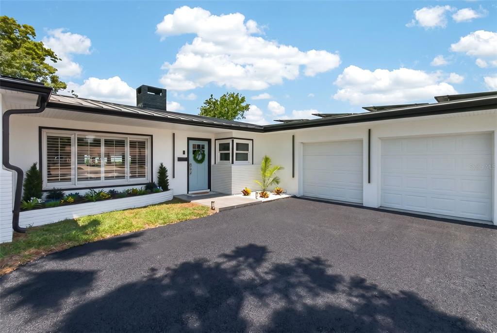 A white single-story house with a black metal roof, two garage doors, and a driveway — 1714 INDIAN ROCKS ROAD, BELLEAIR, FL