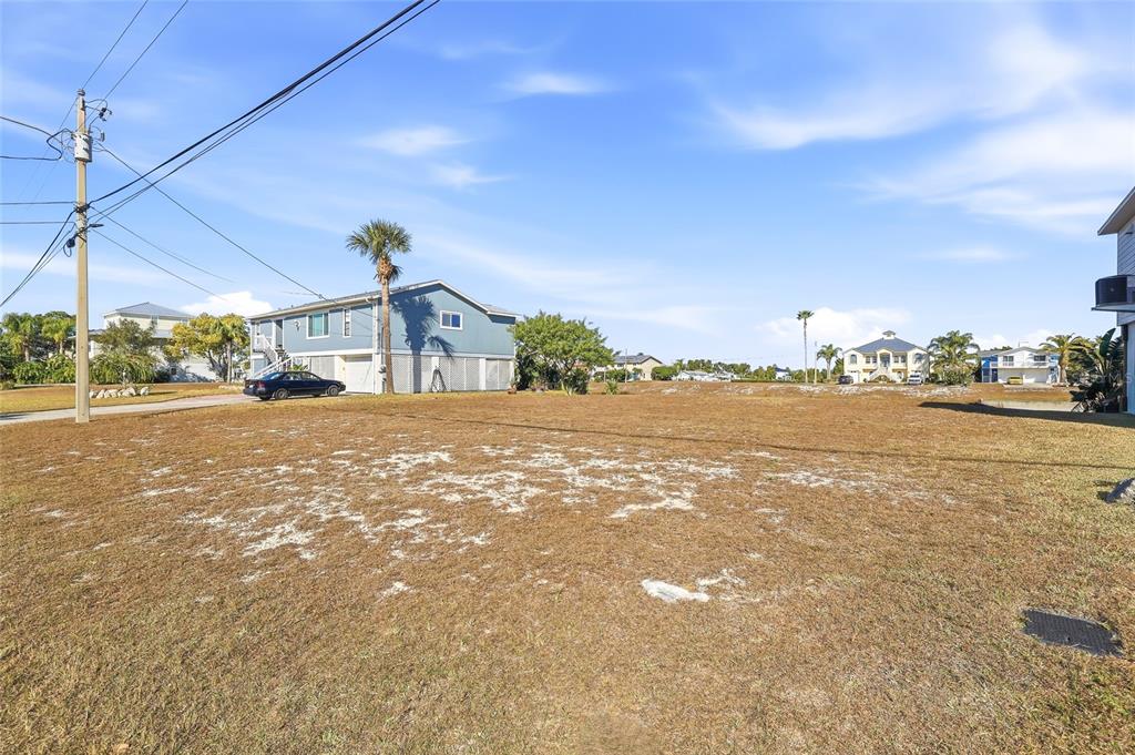 A vacant, grassy lot sits in front of a blue elevated house under a blue sky — 4017 BLUEFISH DRIVE, HERNANDO BEACH, FL