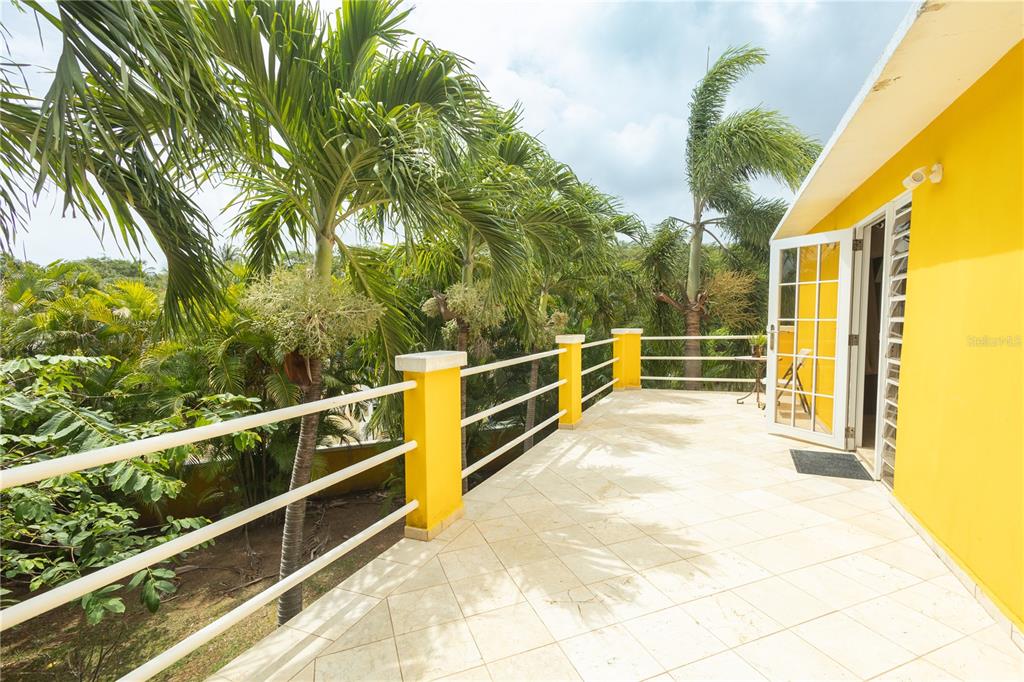 A yellow exterior wall opens onto a tiled balcony with a white railing and palm trees — 615 BRAVOS DE BOSTON, VIEQUES, PR