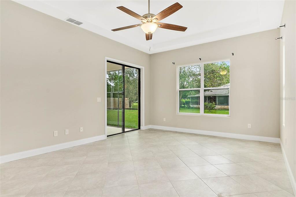 An empty room with light-colored tile floors, a ceiling fan, sliding glass doors, and windows — 3 WHITE HOLLY PLACE, PALM COAST, FL