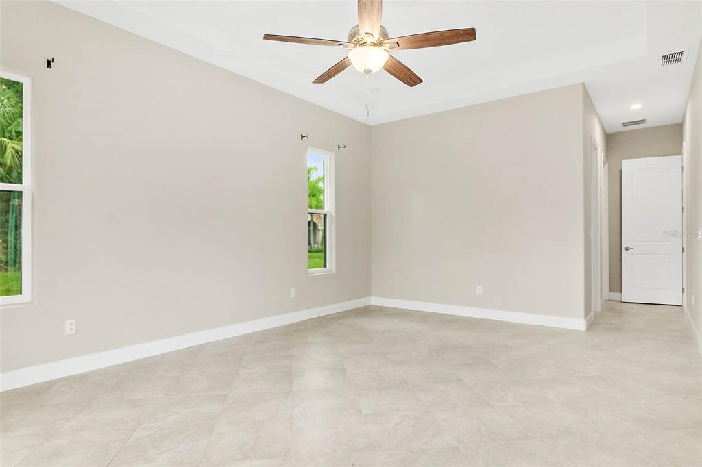 An empty bedroom with light-colored tile flooring, beige walls, a ceiling fan, and two windows — 3 WHITE HOLLY PLACE, PALM COAST, FL