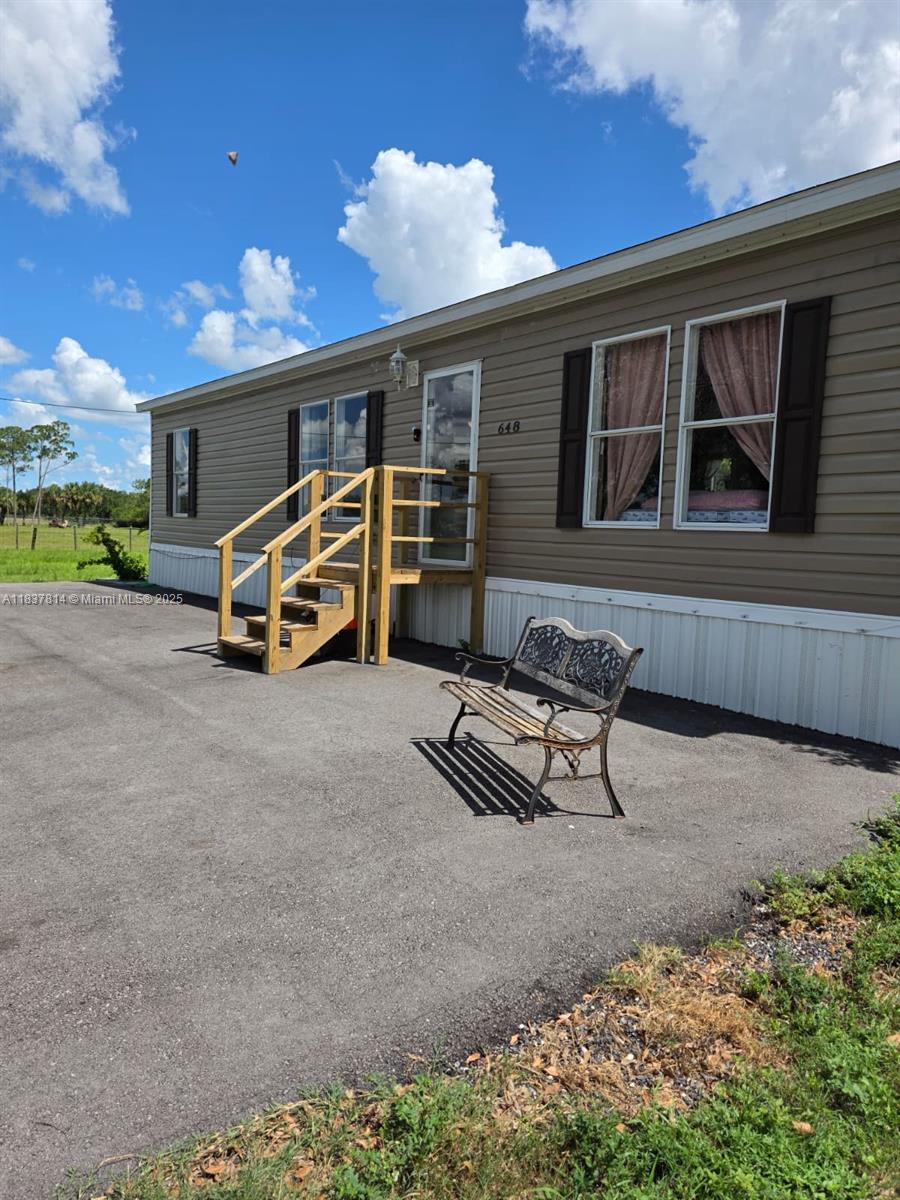 A tan mobile home exterior features a wooden staircase, dark shutters, and a metal bench — 648 Avenida del Sur, Clewiston FL 33440, CLEWISTON, FL