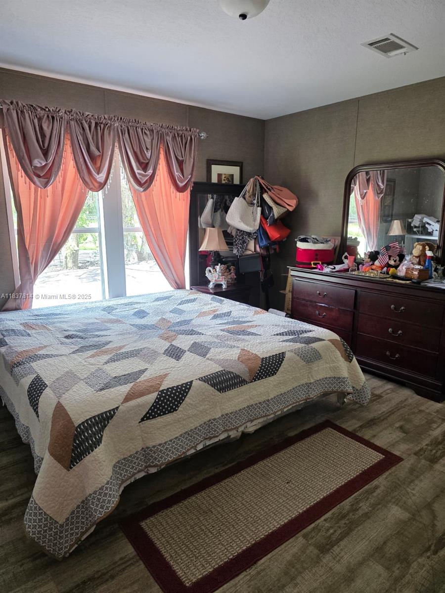 A bedroom features a patterned quilt on the bed, dark wood furniture, and pink curtains — 648 Avenida del Sur, Clewiston FL 33440, CLEWISTON, FL