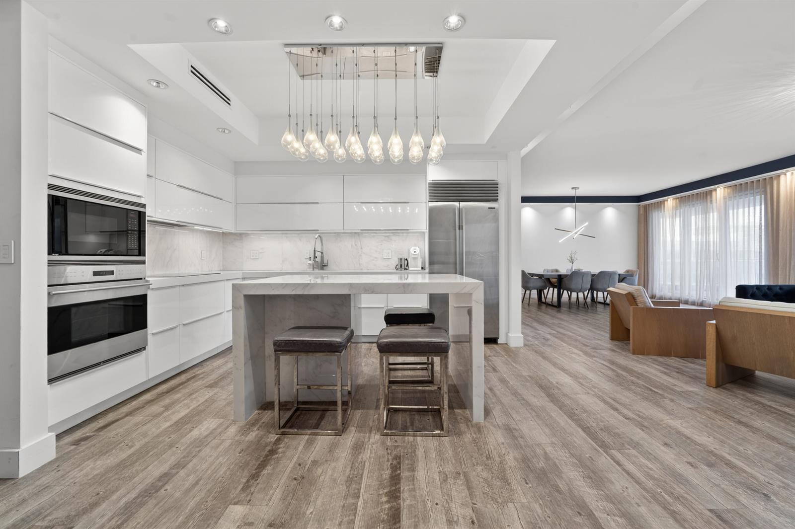 A modern white kitchen features a marble island, stainless steel appliances, and wood-look flooring — 2301 Collins Avenue, Miami Beach FL 33139, MIAMI BEACH, FL