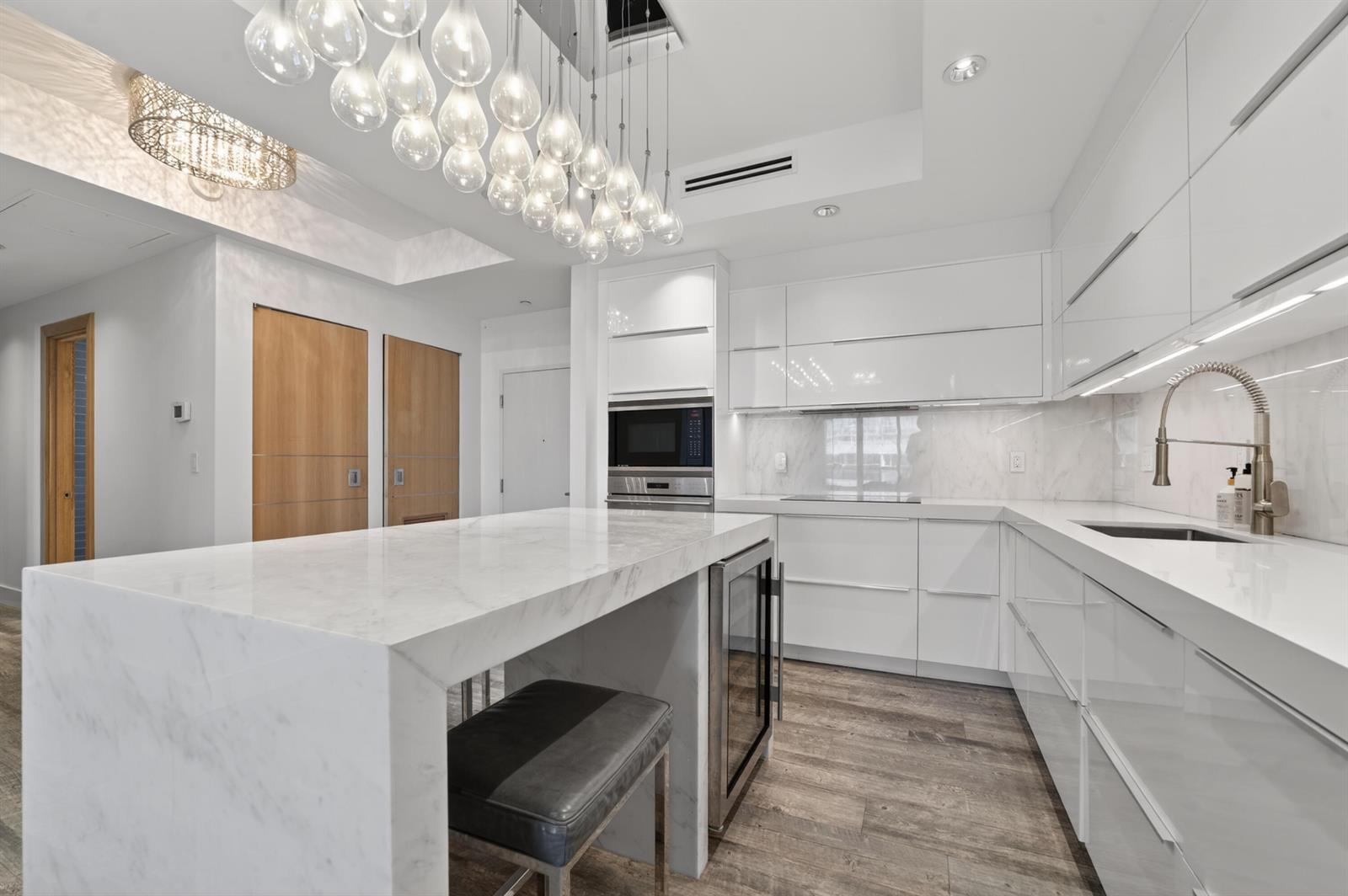 A modern white kitchen features a marble waterfall island, pendant lights, and wood flooring — 2301 Collins Avenue, Miami Beach FL 33139, MIAMI BEACH, FL