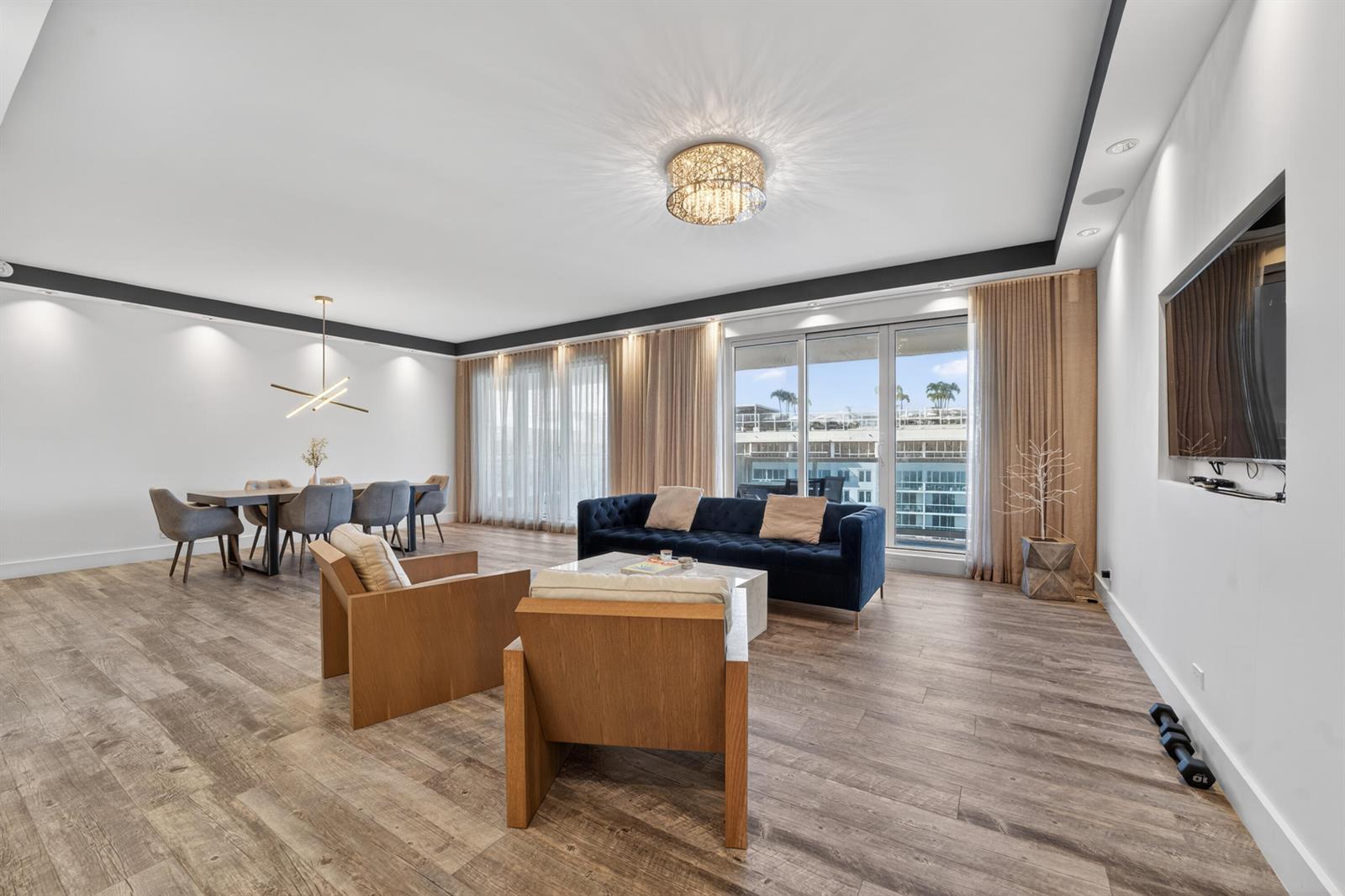 A spacious living and dining room features wood-look flooring, a blue sofa, and balcony access — 2301 Collins Avenue, Miami Beach FL 33139, MIAMI BEACH, FL