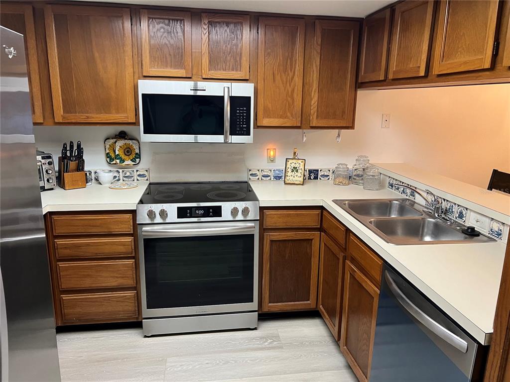 A kitchen features wood cabinets, stainless steel appliances, and a white countertop with tiled backsplash — 333 WOODLAKE WYNDE, OLDSMAR, FL