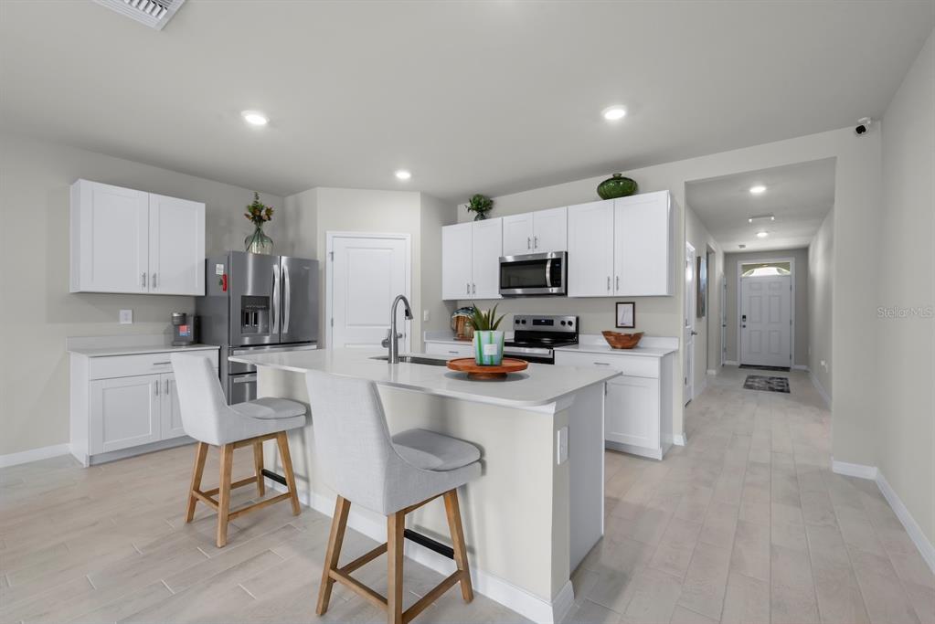 A modern kitchen features white cabinets, stainless steel appliances, a central island, and light flooring — 1422 POWELL VALLEY DRIVE, PORT CHARLOTTE, FL