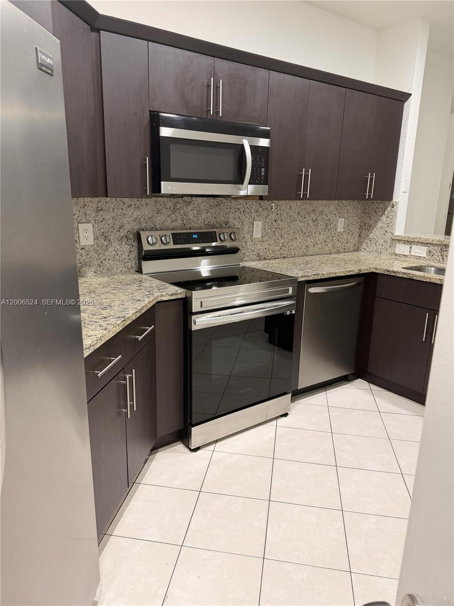 A kitchen features dark wood cabinets, stainless steel appliances, and speckled granite countertops — 9040 NW 54th St, Sunrise FL 33351, SUNRISE, FL