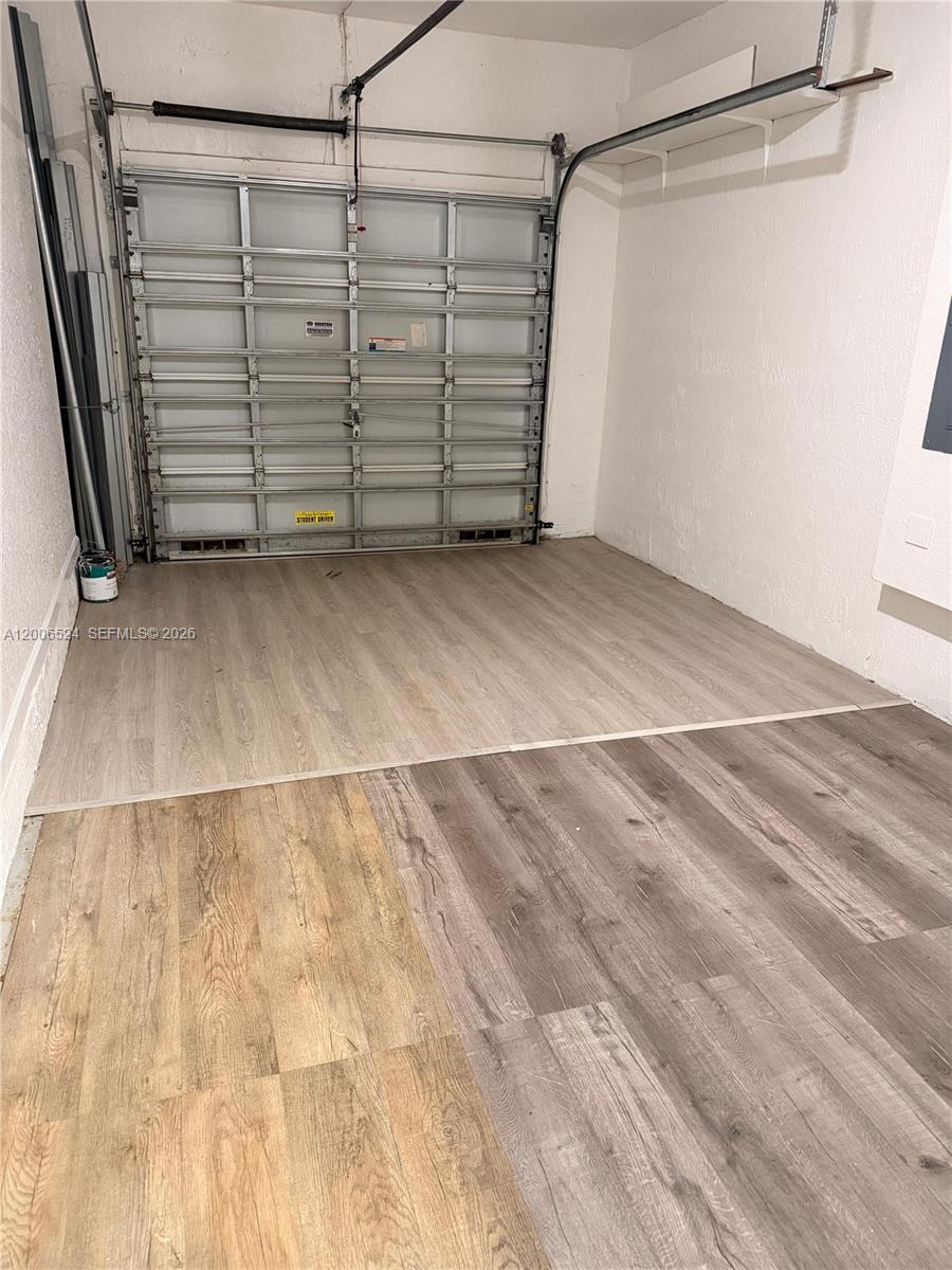 A garage interior features a metal sectional door and mismatched wood-look laminate flooring — 9040 NW 54th St, Sunrise FL 33351, SUNRISE, FL