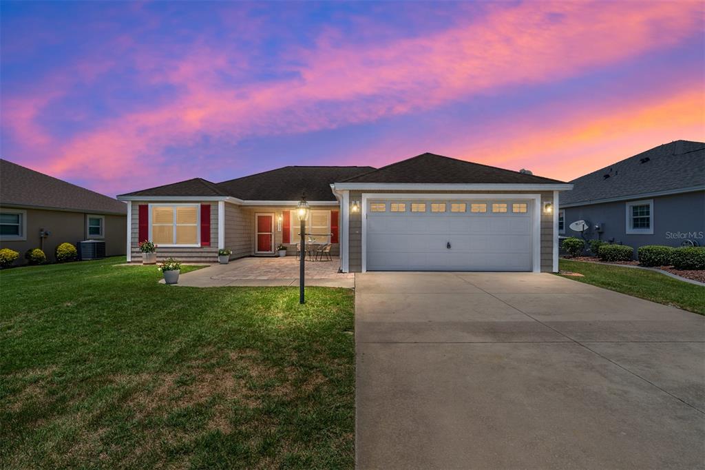A single-story house with a beige exterior, red shutters, and a two-car garage at sunset — 1773 HOLLOW BRANCH WAY, THE VILLAGES, FL
