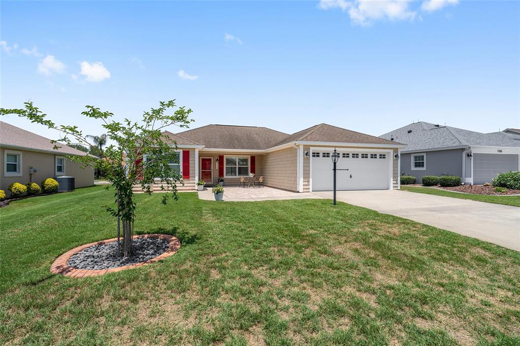A single-story house with a tan exterior, red shutters, and a paved front patio — 1773 HOLLOW BRANCH WAY, THE VILLAGES, FL