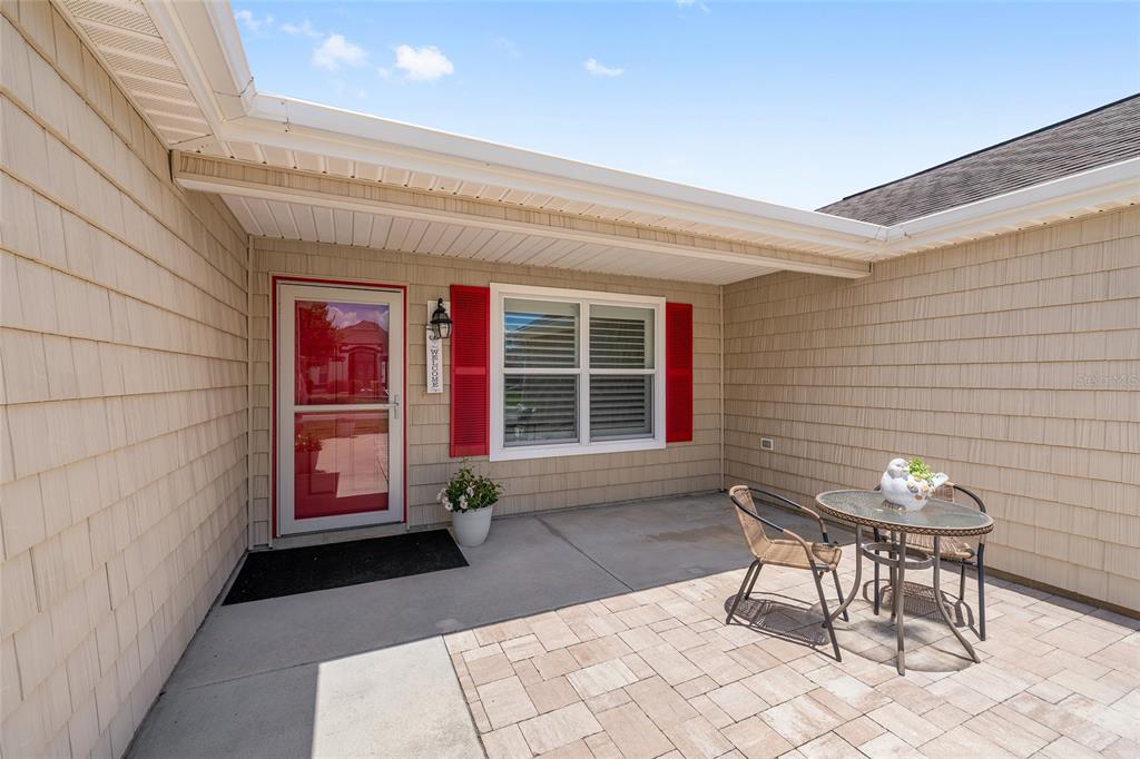A tan shingled house exterior features a red front door, a patio, and outdoor furniture — 1773 HOLLOW BRANCH WAY, THE VILLAGES, FL