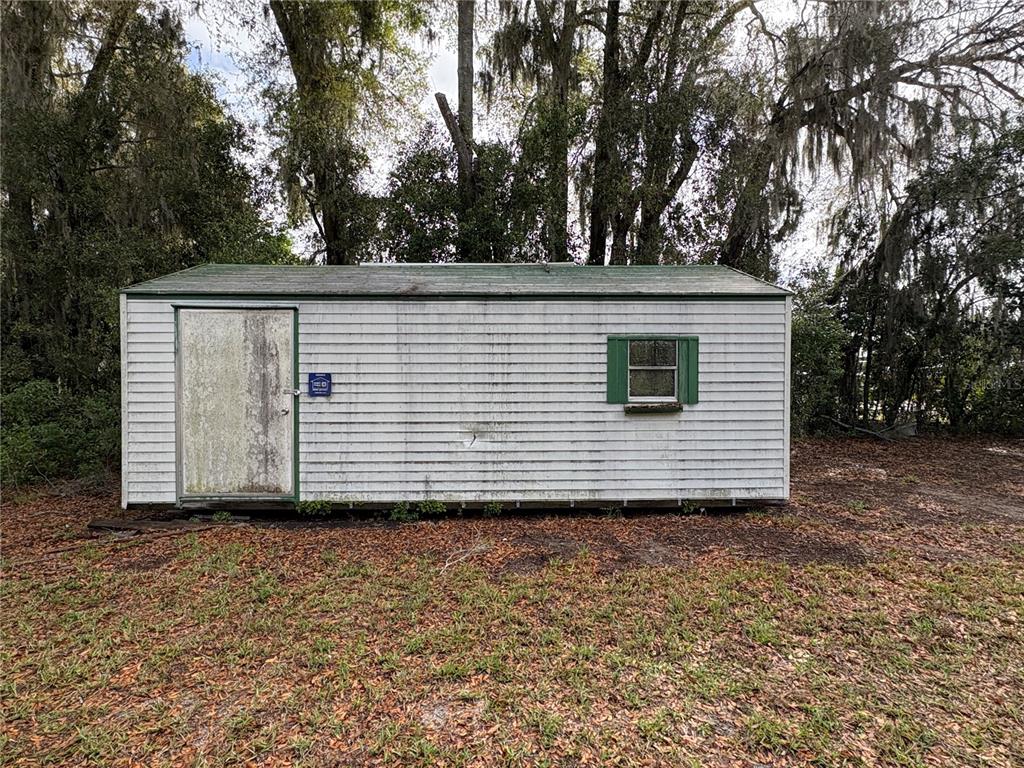 A white, rectangular storage shed with a green roof and a single window sits outdoors — 131 N C 470, LAKE PANASOFFKEE, FL