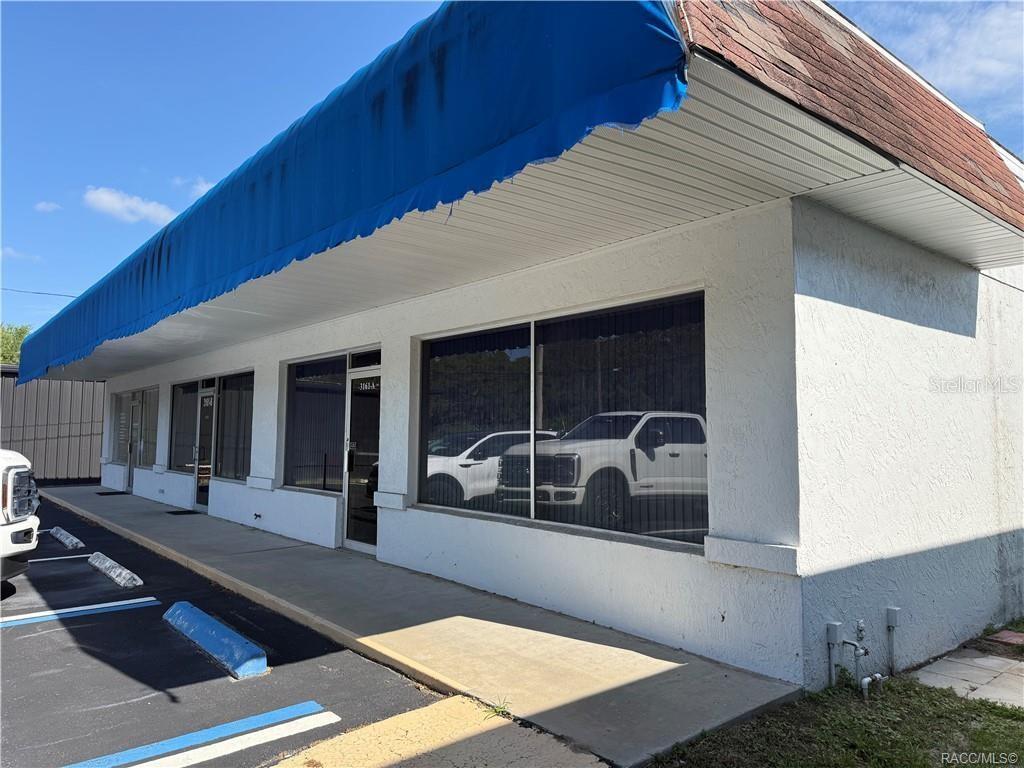A commercial building exterior features a blue awning, white stucco walls, and large glass windows — 3161 E GULF TO LAKE HIGHWAY, INVERNESS, FL