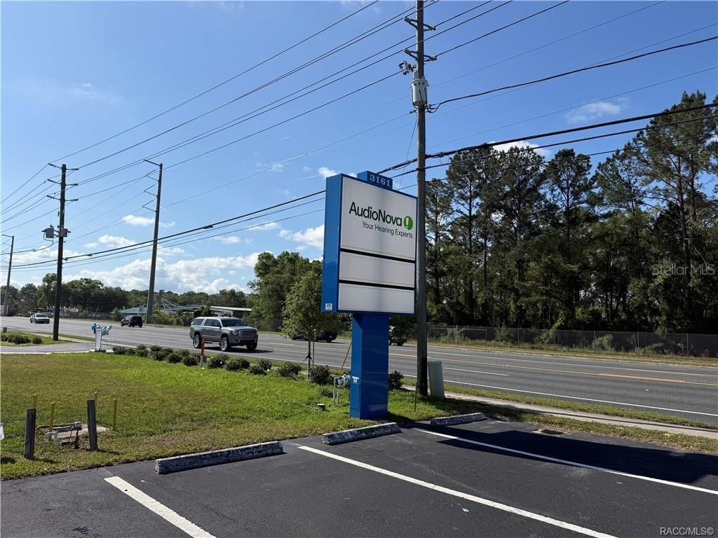 A blue freestanding sign for AudioNova stands in a parking lot beside a road — 3161 E GULF TO LAKE HIGHWAY, INVERNESS, FL