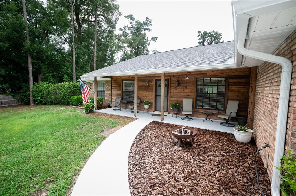 A covered porch with wood siding, outdoor seating, and a fire pit in the yard — 23816 OAK TREE DRIVE, SORRENTO, FL