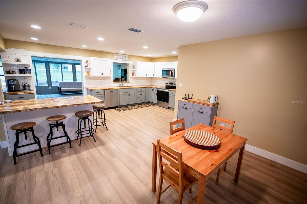 A kitchen with white cabinets, a wood-topped island, and an adjacent dining area — 23816 OAK TREE DRIVE, SORRENTO, FL