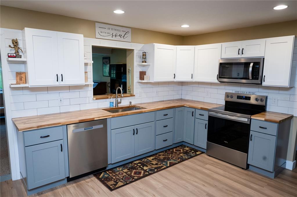 A kitchen features blue lower cabinets, white upper cabinets, wood countertops, and a white backsplash — 23816 OAK TREE DRIVE, SORRENTO, FL