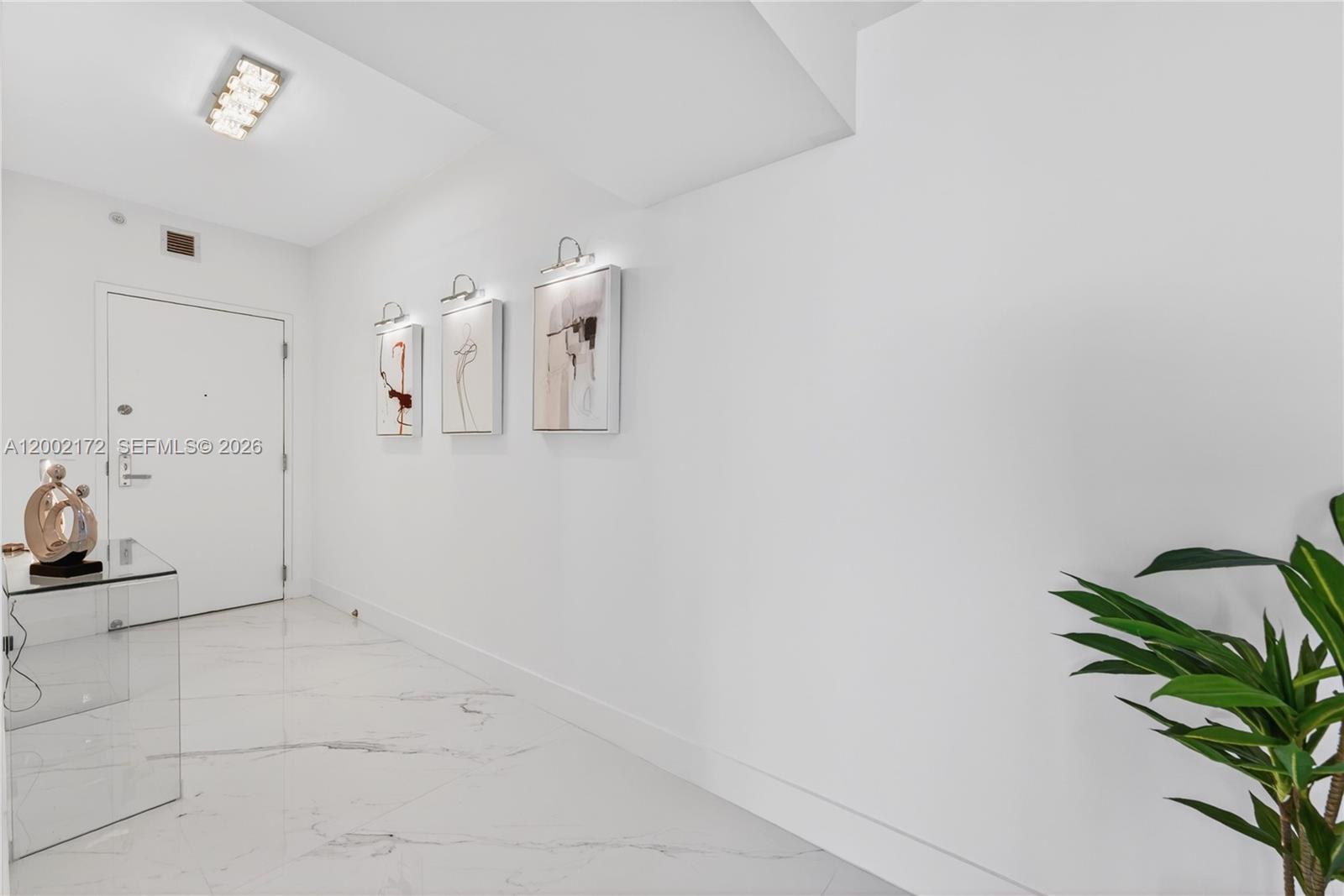 A white hallway features marble floors, three framed wall art pieces, and a glass console table — 888 Biscayne Blvd # 2404, Miami FL 33132, MIAMI, FL