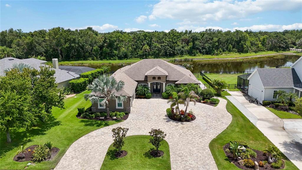 An aerial view shows a single-story house with a paver driveway and a backyard pond — 15415 MULHOLLAND ROAD, PARRISH, FL