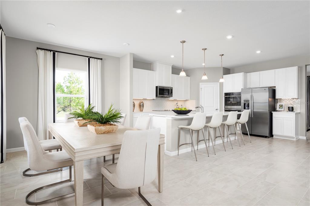 A bright kitchen and dining area features white cabinetry, stainless steel appliances, and tile flooring — 11170 NELLIE CROSSING CIRCLE, CLERMONT, FL