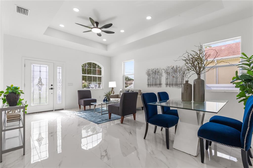 A bright open-concept living and dining area features white tile floors and a tray ceiling — 8314 N PADDOCK AVENUE, TAMPA, FL