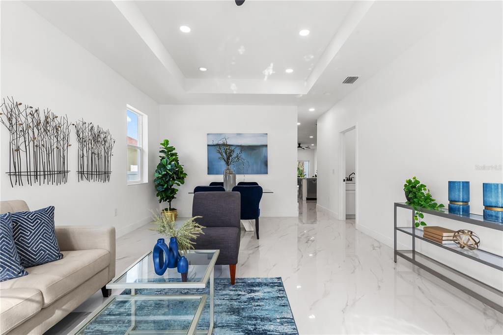 A bright living and dining area features white marble floors, a tray ceiling, and blue accents — 8314 N PADDOCK AVENUE, TAMPA, FL