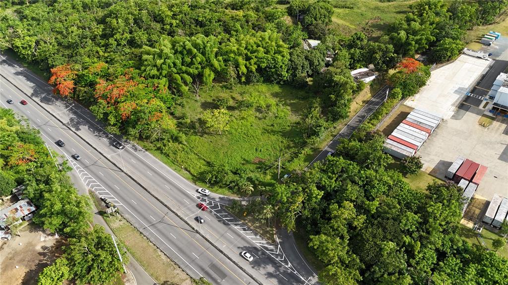 An aerial view shows a vacant grassy lot bordered by a highway and industrial storage area — PR 2 KM 175.4, SAN GERMAN, PR