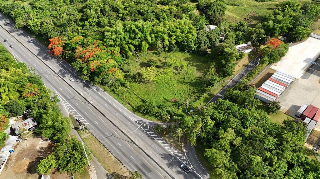 An aerial view shows a grassy lot bordered by a highway, trees, and shipping containers — PR 2 KM 175.4, SAN GERMAN, PR