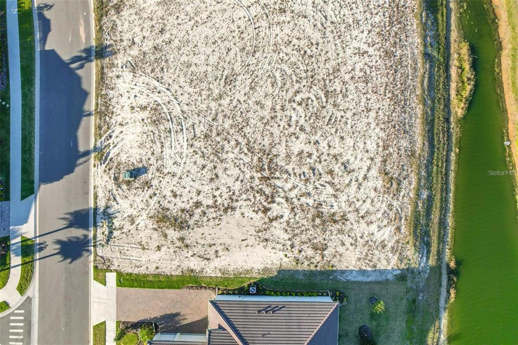An aerial view shows a vacant, sandy residential lot situated between a road and a canal — 130 DEL PALMA DRIVE, PALM COAST, FL