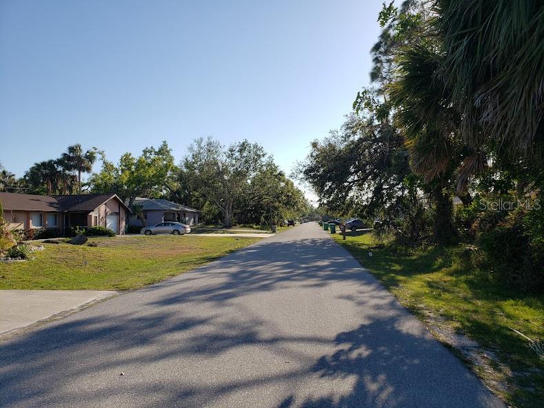 A paved residential street lined with houses, trees, and parked cars under a clear sky — 928 TROPICAL AVENUE NW, PORT CHARLOTTE, FL