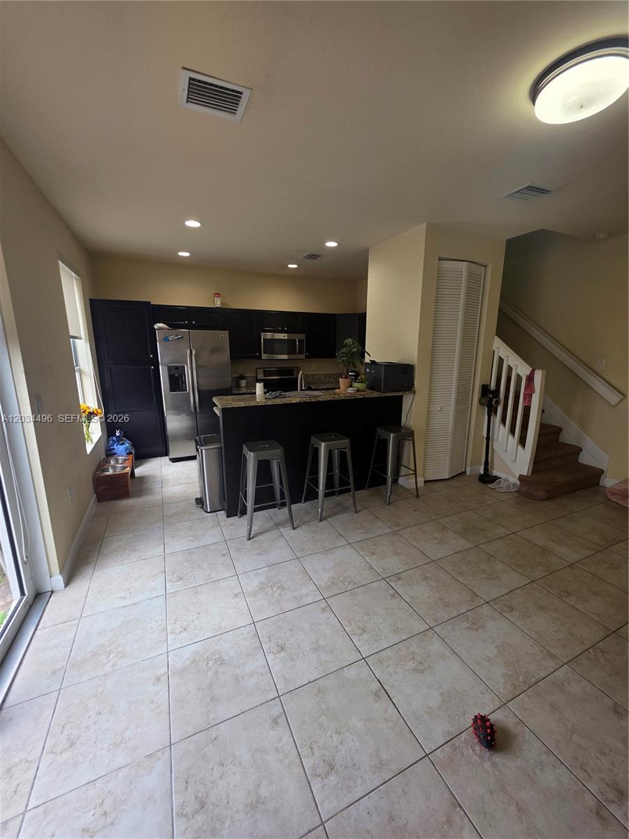 This kitchen features dark cabinets, granite countertops, a breakfast bar with stools, and tile flooring — 9424 SW 171st Pl, Miami FL 33196, MIAMI, FL