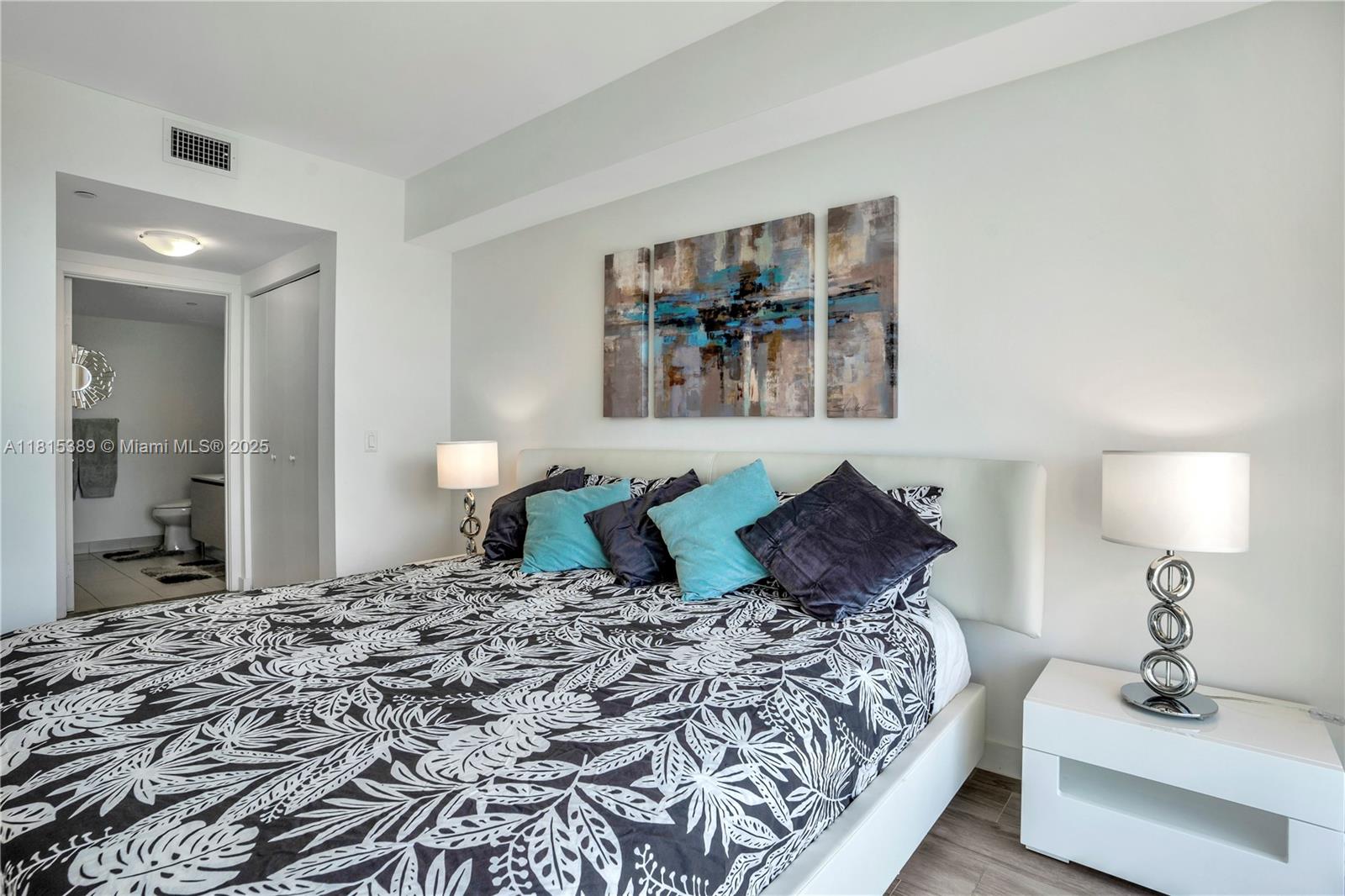 A bedroom features a bed with patterned bedding, two lamps, and a triptych wall art piece — 4250 Biscayne Blvd # 1116, Miami FL 33137, MIAMI, FL