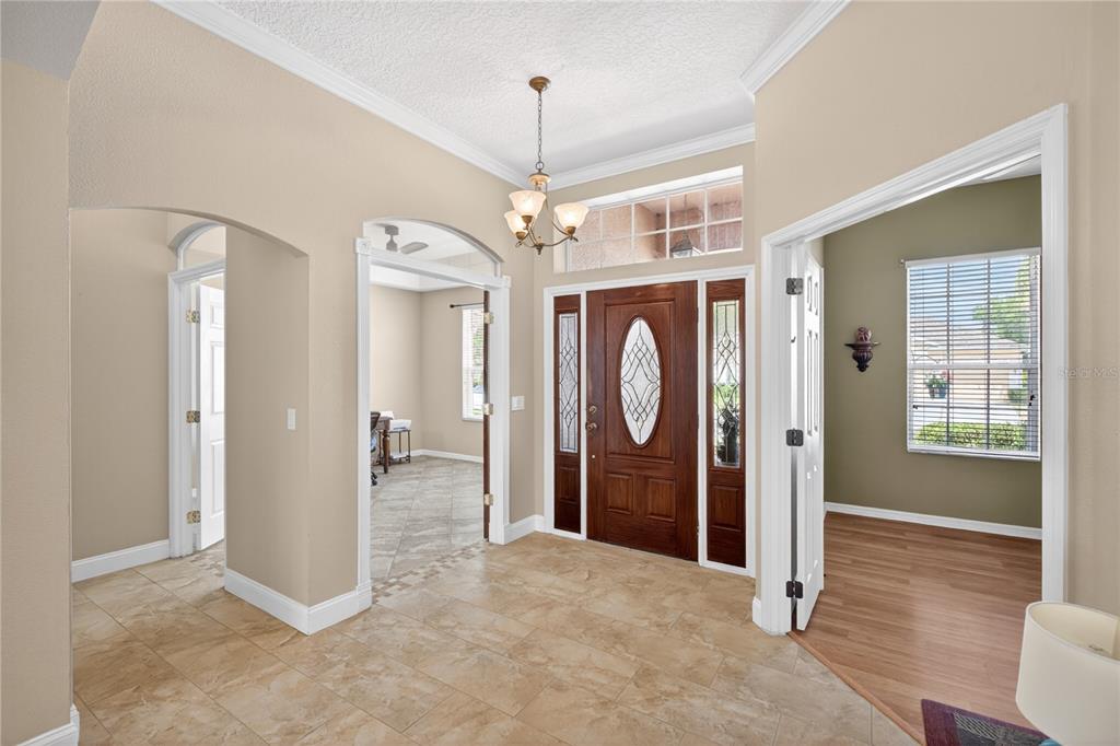 A tiled entryway features a wooden front door, a chandelier, and arched doorways to adjacent rooms — 10174 MALLARD LANDINGS WAY, ORLANDO, FL