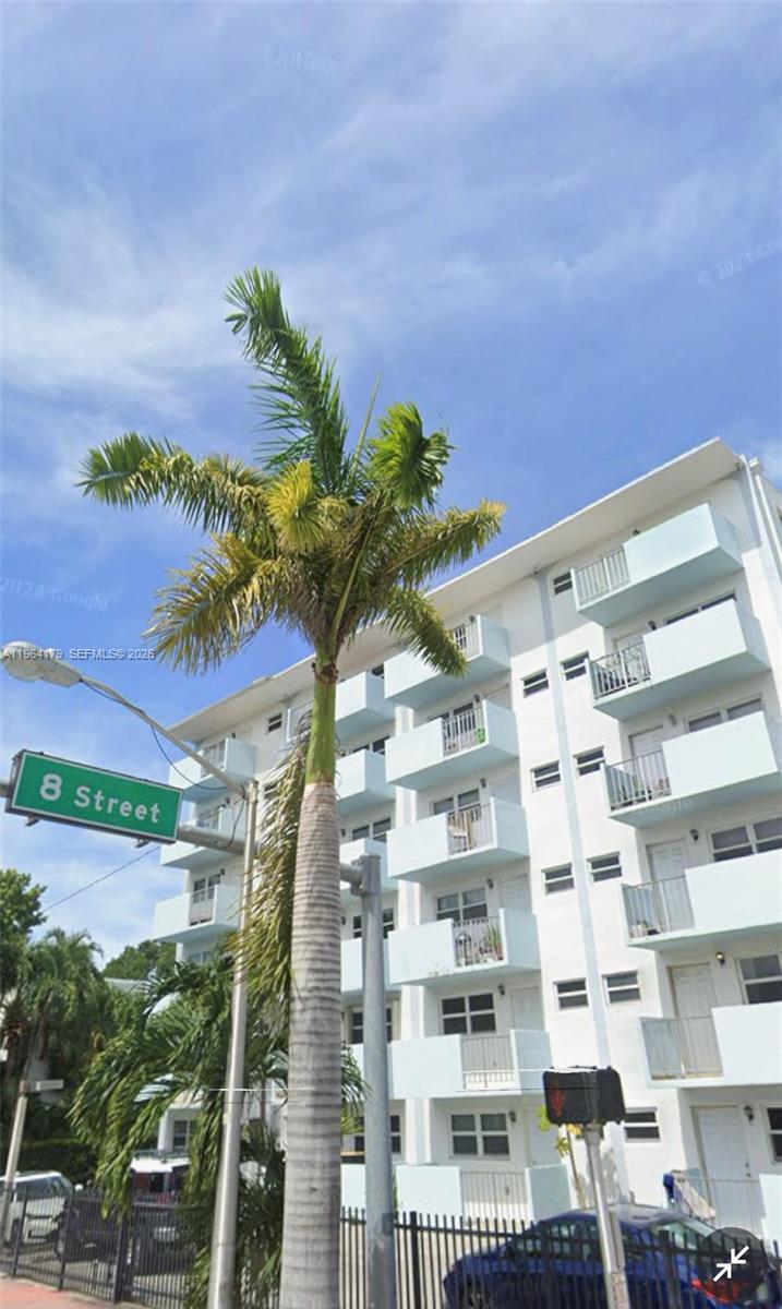 A tall palm tree stands in front of a multi-story white apartment building with balconies — 801 Meridian Ave # 3B, Miami Beach FL 33139, MIAMI BEACH, FL