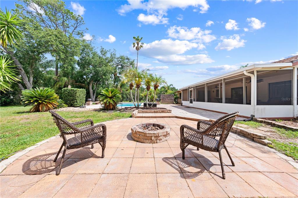 A stone fire pit sits on a paved patio with two wicker chairs and a pool — 2440 CRANE COURT, ST CLOUD, FL
