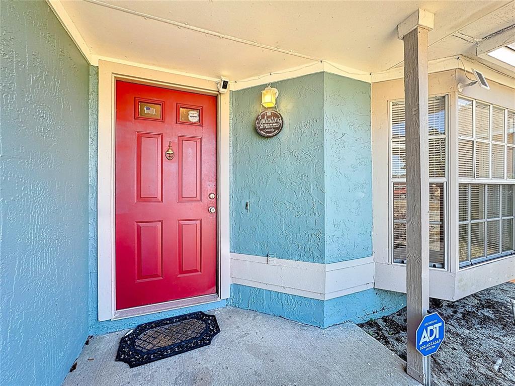 A red front door is set into a light blue stucco wall under a porch — 3717 NARROLINE DRIVE, ORLANDO, FL