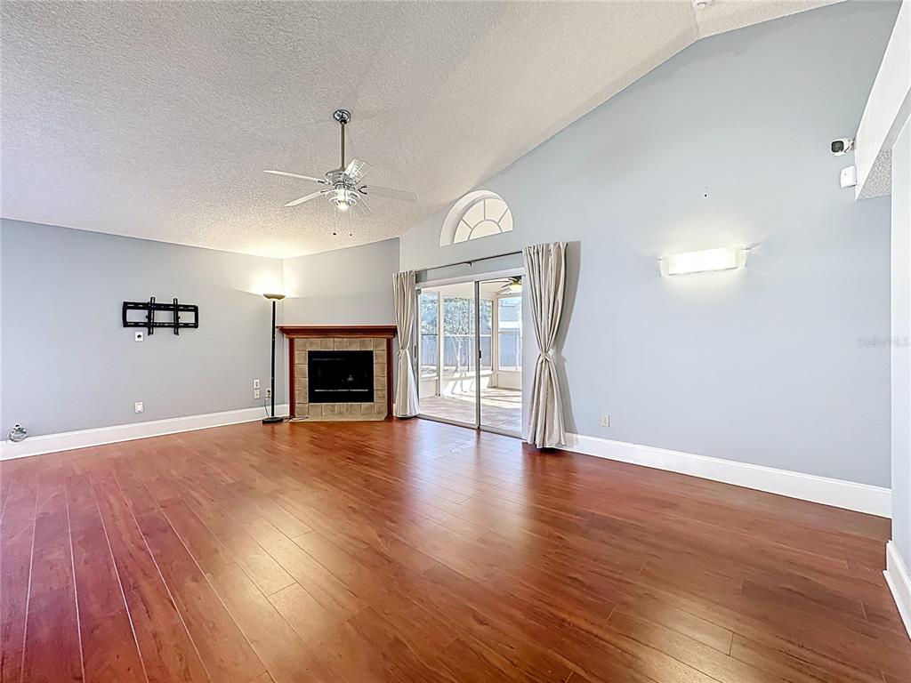 A living room with hardwood floors, a fireplace, vaulted ceilings, and sliding glass doors — 3717 NARROLINE DRIVE, ORLANDO, FL