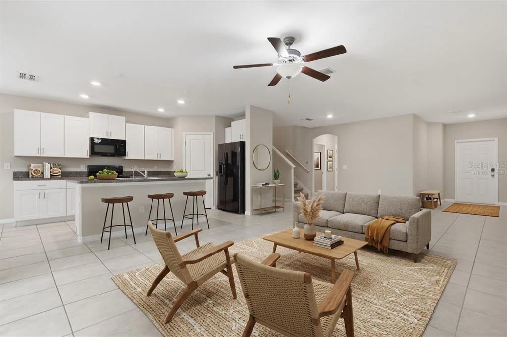 This open-concept living area features a kitchen with white cabinets, an island, and tile flooring — 7023 SAMUEL IVY DRIVE, TAMPA, FL