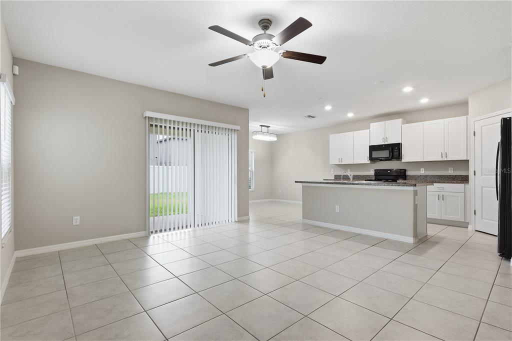 An open-concept kitchen and dining area with white cabinets, tile flooring, and sliding glass doors — 7023 SAMUEL IVY DRIVE, TAMPA, FL