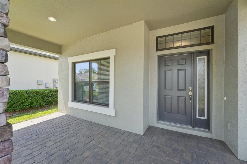 A covered entryway features a dark gray front door, a window, and brick paver flooring — 1741 CHERRY WALK ROAD, LUTZ, FL