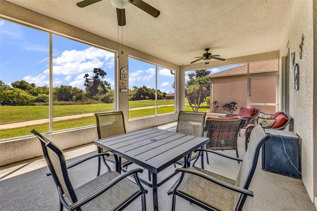 A screened-in patio features a dining set, outdoor seating, and views of a grassy field — 24376 WESTGATE BOULEVARD, PUNTA GORDA, FL