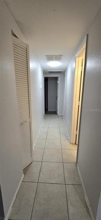 A hallway with light-colored tile flooring, white walls, and louvered closet doors — 21440 MIDWAY BOULEVARD, PORT CHARLOTTE, FL